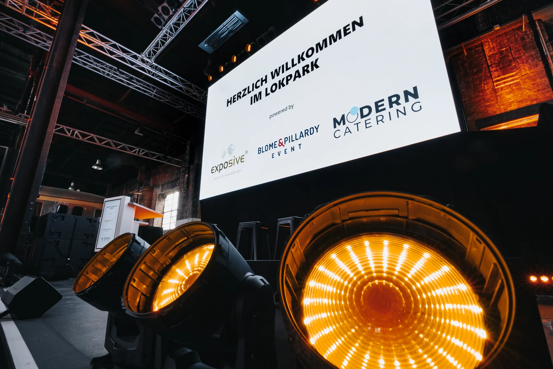 Beleuchtete Bühne im Lokpark mit Willkommensleinwand und Modern Catering Logo